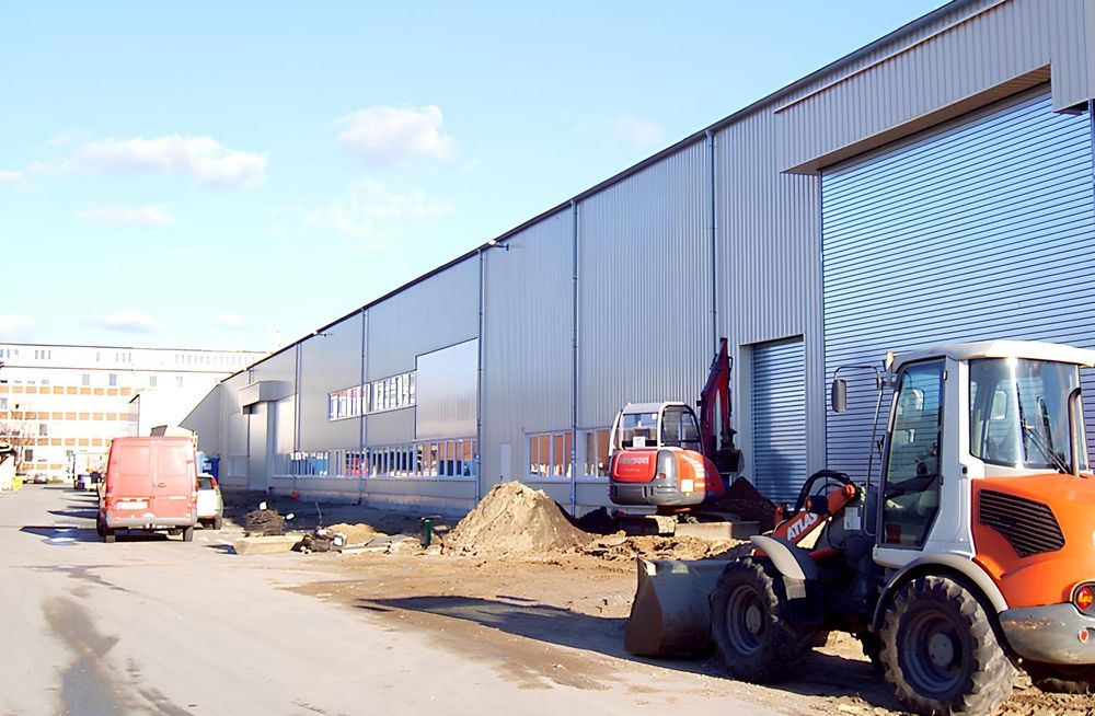 Baustelle mit Baggern vor einer neuen Industriehalle mit Metallverkleidung